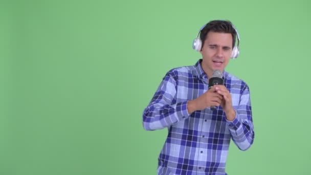 Happy young handsome hipster man listening to music and singing with microphone — Stock Video