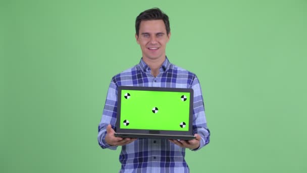 Счастливый молодой красивый хипстер показывает ноутбук и выглядит удивленным — стоковое видео