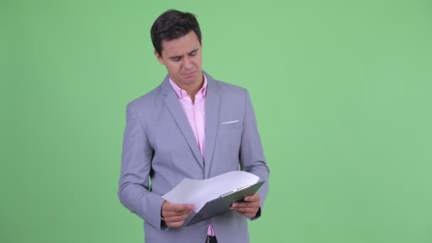 Happy young handsome businessman talking while holding clipboard — Stock Video