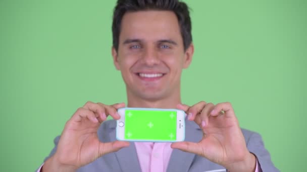 Face of happy young handsome businessman thinking while showing phone — Stock Video