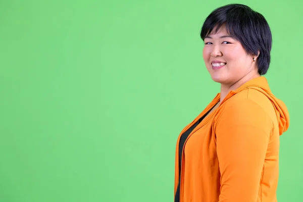 Profil-Ansicht der jungen glücklichen übergewichtigen asiatischen Frau, die in die Kamera schaut, bereit für das Fitnessstudio — Stockfoto