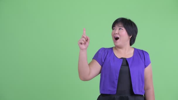 Счастливая молодая толстая азиатка указывает вверх и выглядит удивленной. — стоковое видео