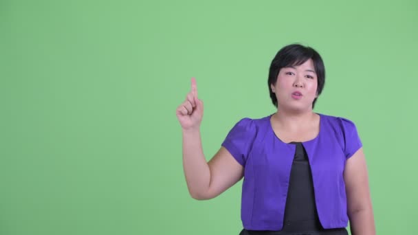 Feliz jovem mulher asiática com sobrepeso apontando para cima e falando — Vídeo de Stock
