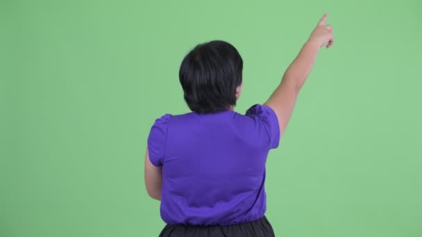 Вид сзади на молодую толстую азиатку, указывающую пальцем — стоковое видео