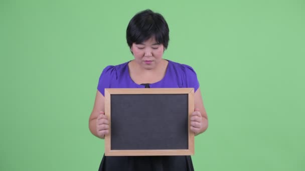 Щаслива молода надмірна вага Азіатська жінка думає при проведенні дошки — стокове відео