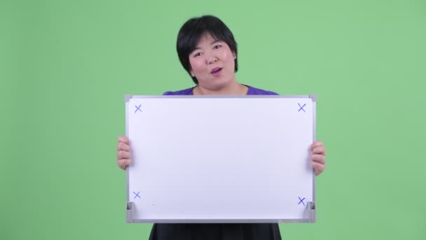 Feliz joven mujer asiática con sobrepeso hablando mientras sostiene la pizarra blanca — Vídeos de Stock