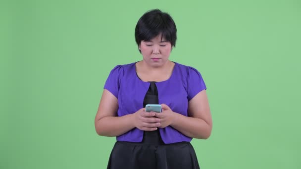 Glücklich junge übergewichtige asiatische Frau wartet, während mit dem Telefon — Stockvideo