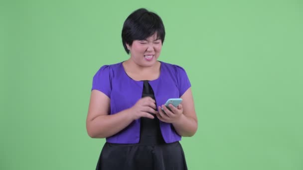 Feliz joven mujer asiática con sobrepeso usando el teléfono y recibiendo buenas noticias — Vídeo de stock
