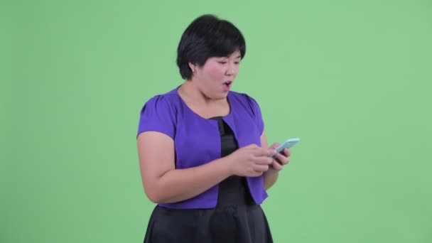 快乐的年轻超重亚洲妇女使用手机，看起来惊讶 — 图库视频影像