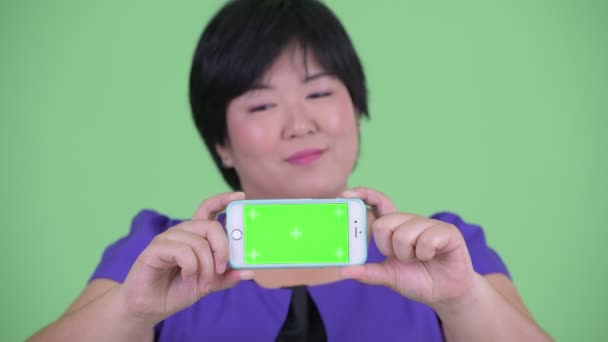幸せな若い太りすぎのアジアの女性の顔思考と携帯電話を示しています — ストック動画
