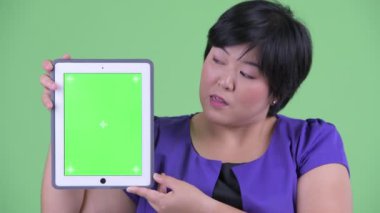 Dijital tablet gösterirken konuşan mutlu genç kilolu Asyalı kadının yüzü
