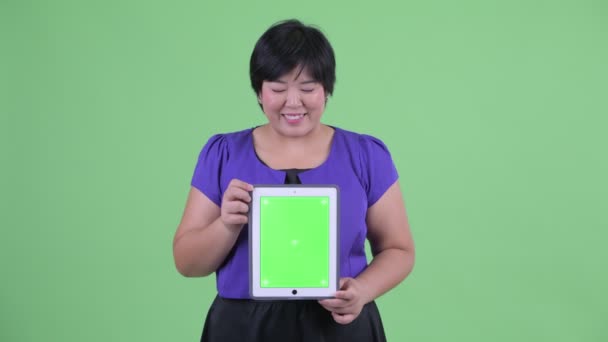 Счастливая молодая толстая азиатка думает, показывая цифровой планшет — стоковое видео