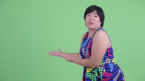 Gelukkig jong overgewicht Aziatische vrouw tonen aan rug en op zoek verrast — Stockvideo