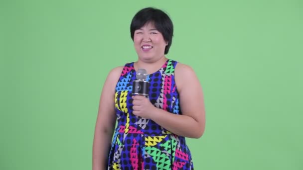 Счастливая молодая азиатка с избыточным весом подарит микрофон — стоковое видео