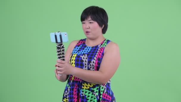 Щаслива молода надмірна вага Азіатська жінка ввході і показуючи телефон готовий до партії — стокове відео