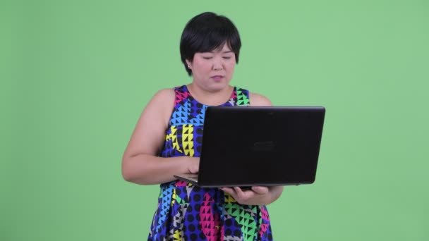 Szczęśliwy młody nadwaga Asian kobieta myślący podczas przy użyciu laptop — Wideo stockowe