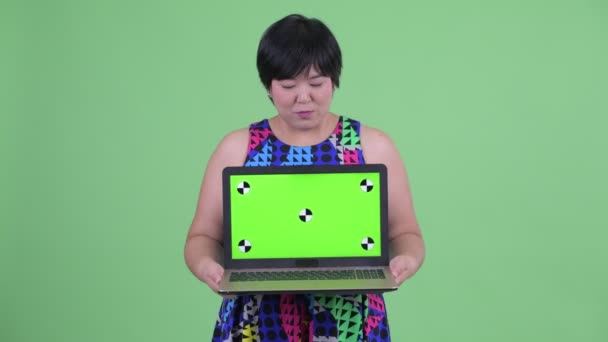 Счастливая молодая толстая азиатка показывает ноутбук и выглядит удивленной — стоковое видео