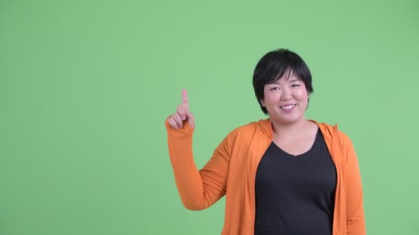 Gelukkig jong overgewicht Aziatische vrouw praten en wijzend omhoog klaar voor sportschool — Stockvideo