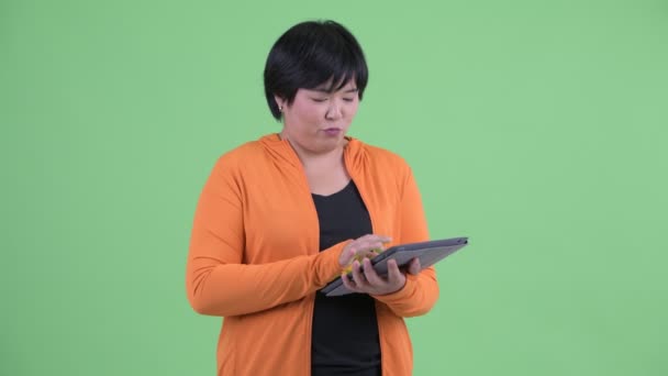 Šťastná mladá nadváha asijská žena přemýšlí, když používá digitální tablet připravený pro tělocvičnu — Stock video