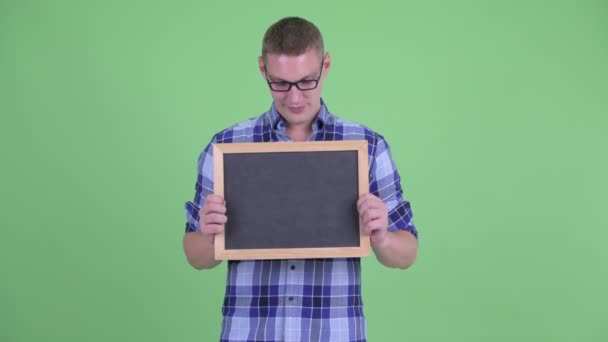 Glücklicher junger Hipster-Mann denkt, während er die Tafel hält — Stockvideo