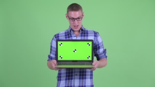 Feliz joven hipster hombre mostrando el ordenador portátil y mirando sorprendido — Vídeos de Stock