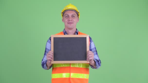 Mutlu genç adam inşaat işçisi kara tahta tutarken konuşurken — Stok video