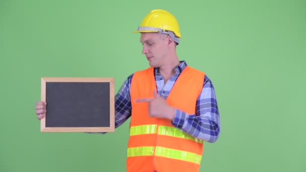 Happy young man construction worker holding blackboard and giving thumbs up — Stock Video