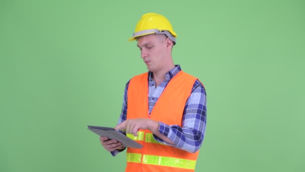 Счастливый молодой человек строитель думает, используя цифровой планшет — стоковое видео