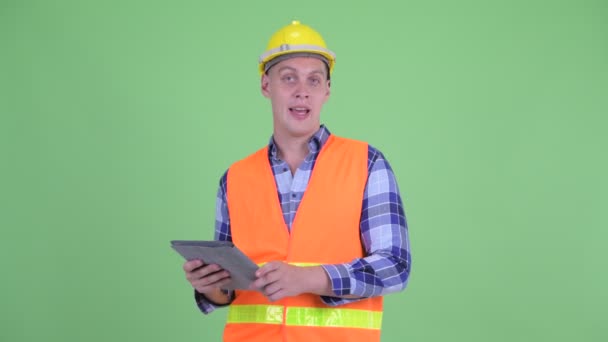 Счастливый молодой человек строитель говорить во время использования цифрового планшета — стоковое видео