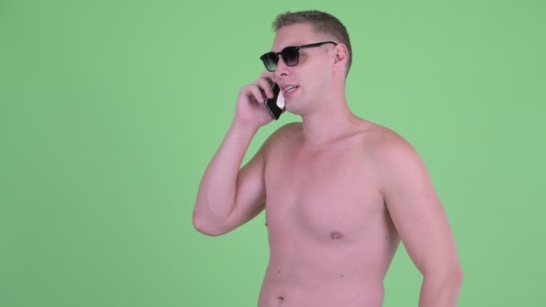 Feliz joven sin camisa hablando por teléfono y quitándose las gafas de sol — Vídeos de Stock