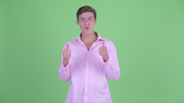 Счастливый молодой привлекательный бизнесмен, подающий большие пальцы и выглядящий взволнованным — стоковое видео