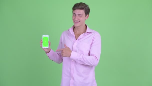 Boldog fiatal üzletember beszél, miközben bemutatja telefon — Stock videók