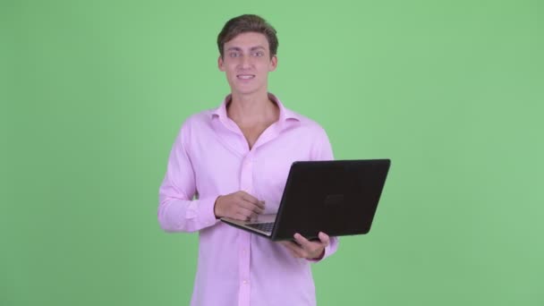 Jovem empresário bonito feliz falando ao usar laptop — Vídeo de Stock