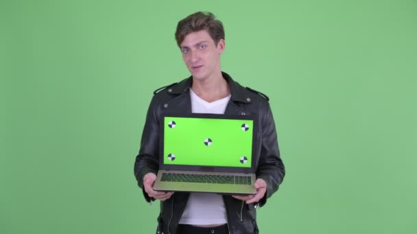 Jovem homem rebelde feliz falando enquanto mostra laptop — Vídeo de Stock