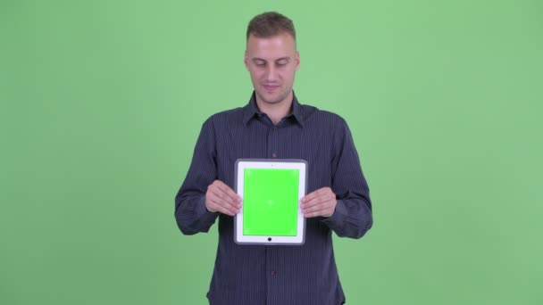Счастливый красивый бизнесмен думает, показывая цифровой планшет — стоковое видео