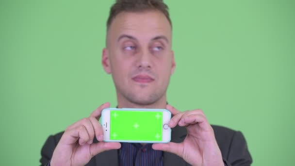 Лицо счастливого привлекательного бизнесмена в костюме, показывающего телефон — стоковое видео