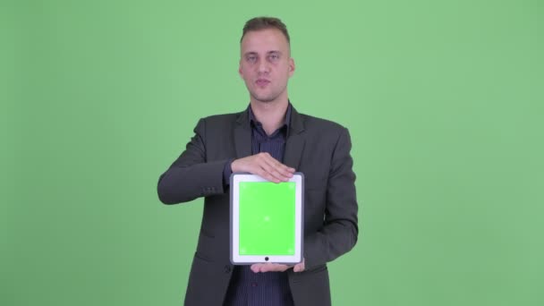 Feliz hombre de negocios guapo en traje hablando mientras muestra tableta digital — Vídeos de Stock