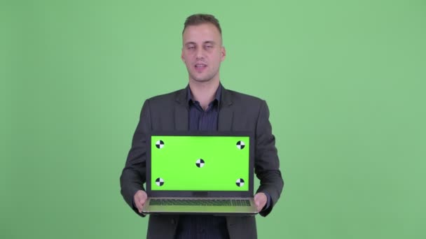 Feliz hombre de negocios guapo en traje hablando mientras muestra el ordenador portátil — Vídeos de Stock