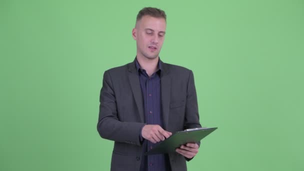 Happy handsome businessman in suit pointing while holding clipboard — Stock Video