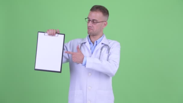 Hombre estresado médico mostrando portapapeles y dando pulgares hacia abajo — Vídeo de stock