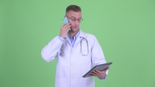 Ευτυχισμένος όμορφος άντρας γιατρός μιλάει στο τηλέφωνο, ενώ χρησιμοποιεί το ψηφιακό δισκίο — Αρχείο Βίντεο