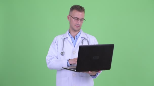 Feliz hombre guapo médico pensando mientras se utiliza el ordenador portátil — Vídeos de Stock