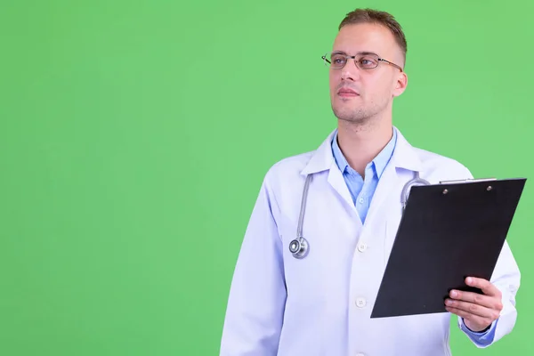 Hombre guapo médico pensando mientras sostiene portapapeles —  Fotos de Stock