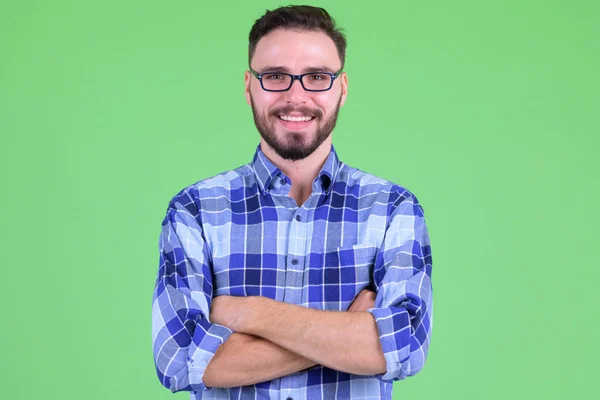 Feliz jovem homem hipster barbudo sorrindo com os braços cruzados — Fotografia de Stock