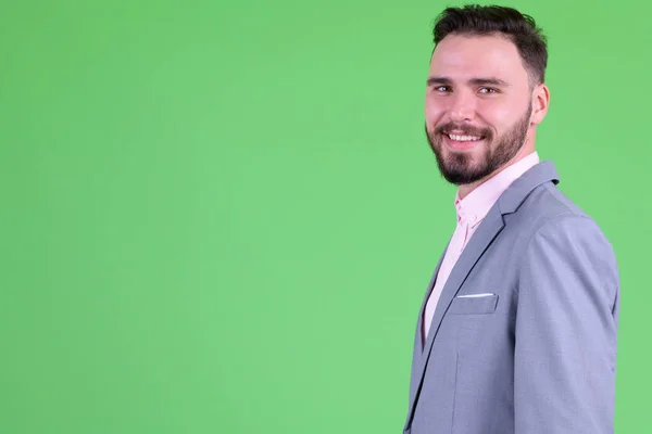 Profiel weergave van Happy Young bebaarde zakenman die naar de camera kijkt — Stockfoto