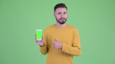 Mutlu genç yakışıklı sakallı adam telefon gösteren ve başparmak veren