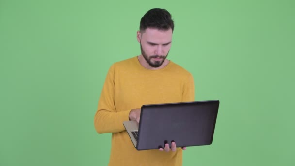 Ευτυχισμένος νέος όμορφος άντρας με γένια χρησιμοποιώντας φορητό υπολογιστή — Αρχείο Βίντεο