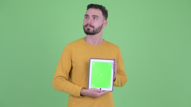 Heureux jeune homme barbu beau penser tout en montrant tablette numérique — Video