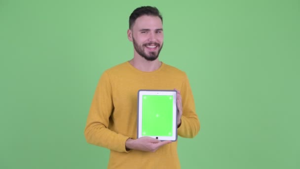 Щасливий молодий красивий бородатий чоловік говорить, показуючи цифровий планшет — стокове відео