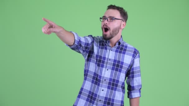 Glücklicher junger bärtiger Hipster-Mann zeigt mit dem Finger und sieht überrascht aus — Stockvideo